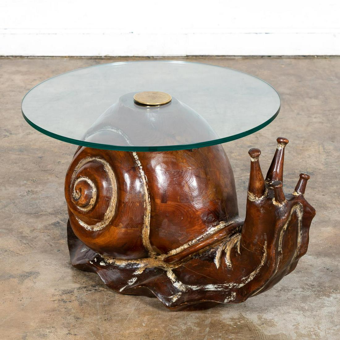 FEDERICO ARMIJO CARVED SNAIL FORM COFFEE TABLE: Federico Armijo (American, b. 1948-), third quarter 20th century. Carved wood coffee table in snail form base and round glass top with brass center. Apparently unmarked. Approx. h. 18", w. 31, diam. o