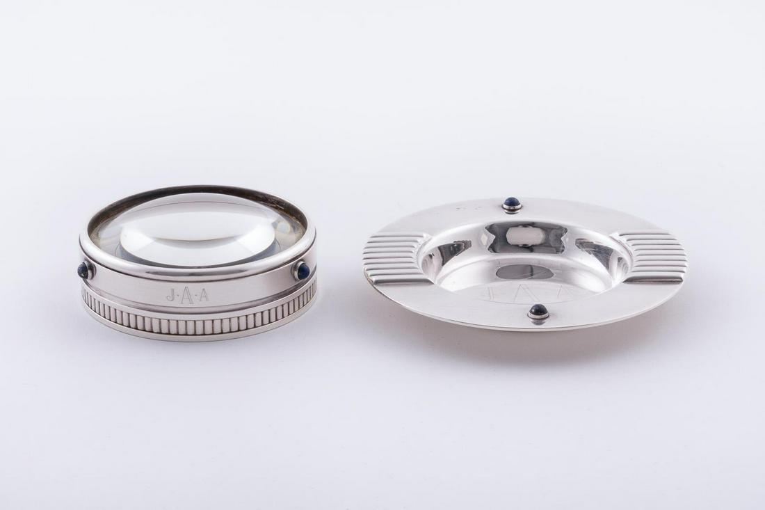 2 CARTIER DESK ACCESSORIES WITH LAPIS ACCENTS: Cartier, late 20th century. Group of silver tone desk accessories comprising of one small round dish with gadrooned sides and lapis stones, and one magnifying lens with blue lapis accent stones. Maker