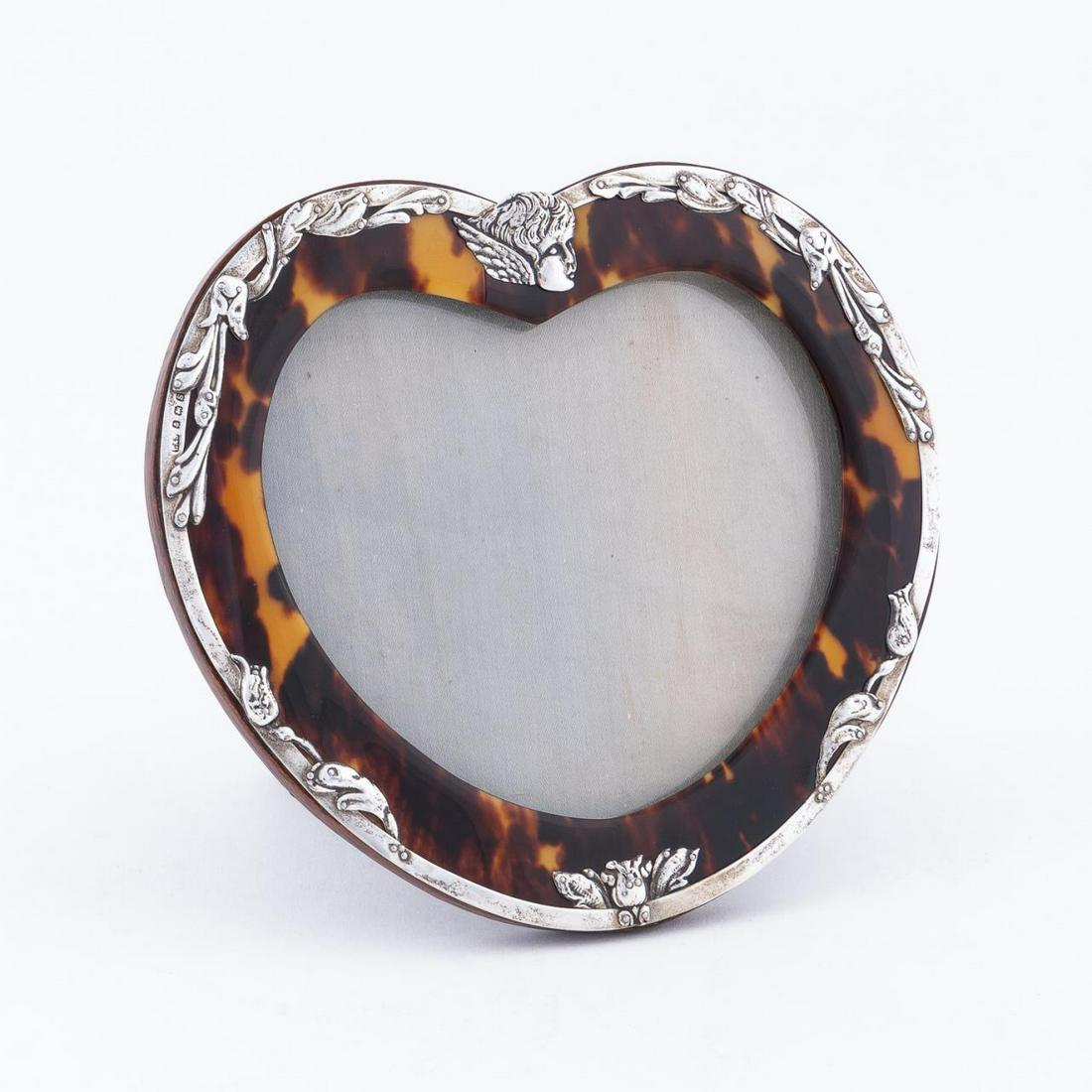 LEVI & SALAMAN, ENGLISH SILVER MOUNTED FRAME: Levi & Salaman (English, 1870-1920), circa 1917. A heart shaped picture frame with sterling silver mounted having hand chased floral and foliate motifs and a winged cherub head to upper crest. Marked 