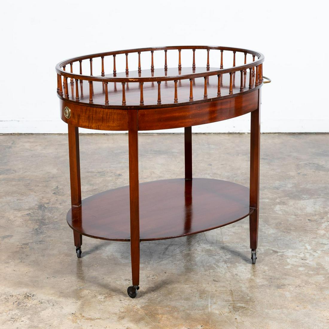 OVAL MAHOGANY ROLLING BAR CART: Likely American, 20th century. Oval form mahogany bar/tea cart or trolley having a gallery rail, single drawer, and shelf below. Unmarked. Approx. h. 34.5", w. 35.75", d. 26".