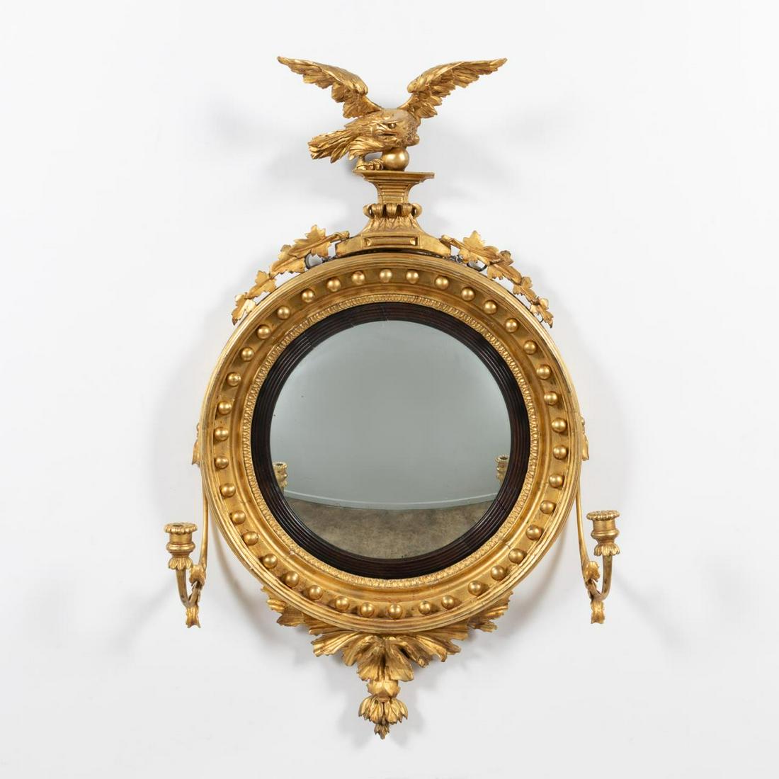 GILTWOOD FEDERAL STYLE CONVEX EAGLE MIRROR, 19TH C: English or American, 19th Century. Federal style gilt framed convex mirror with spread-wing eagle crest, the round mirror with reeded mahogany liner with surrounding spheres, side mounted single candl