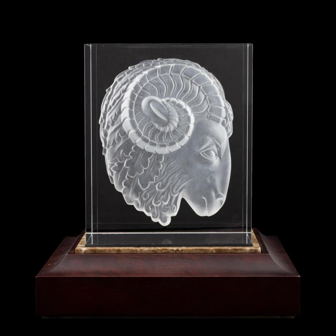 STEUBEN CRYSTAL RAM'S HEAD SCULPTURE ON STAND: Steuben Glass Works, 20th century. Ram's head sculpture, crystal block with a concave acid etched figure of a ram's head accompanied by wood base. Etched "Steuben" to underside. Approx. h. 6.75", w. 5