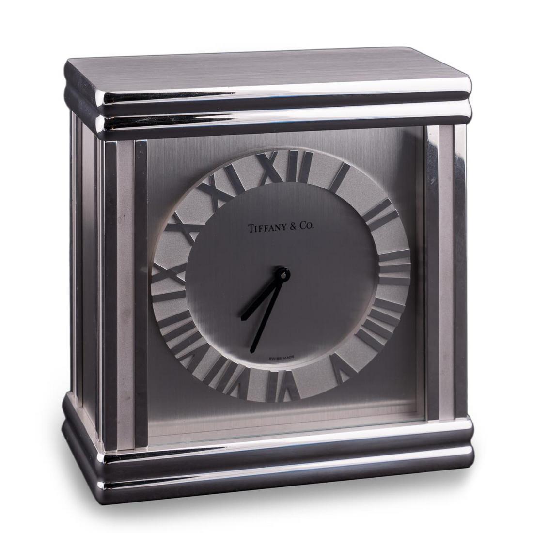 TIFFANY & CO. "ATLAS" MANTEL CLOCK: Tiffany & Co., 20th century. "Atlas" mantel clock in rhodium finish with Roman numeral dial and hinged door revealing Swiss quartz movement. Maker's mark to front and back, and serial number 215885. A