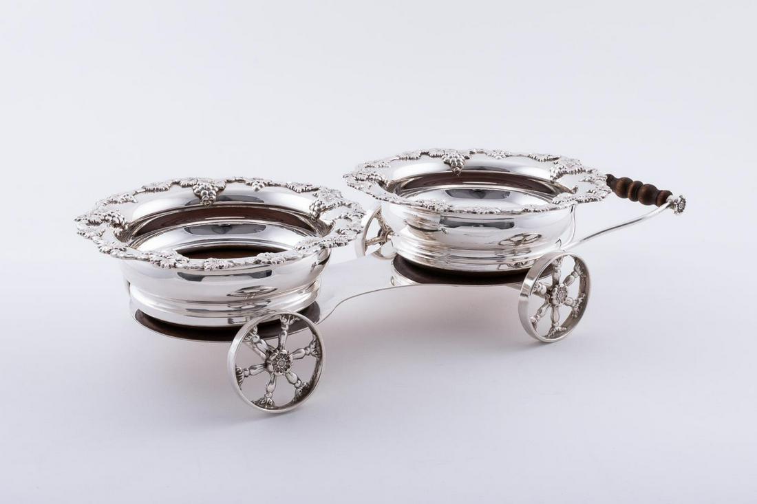 SILVERPLATE DOUBLE COASTER WINE BOTTLE TROLLY: English silver plated double coaster wine bottle coaster wine bottle trolly with repousse' grape motif on upper bowl. Approx. L. 20"m W. 8", H. 4"