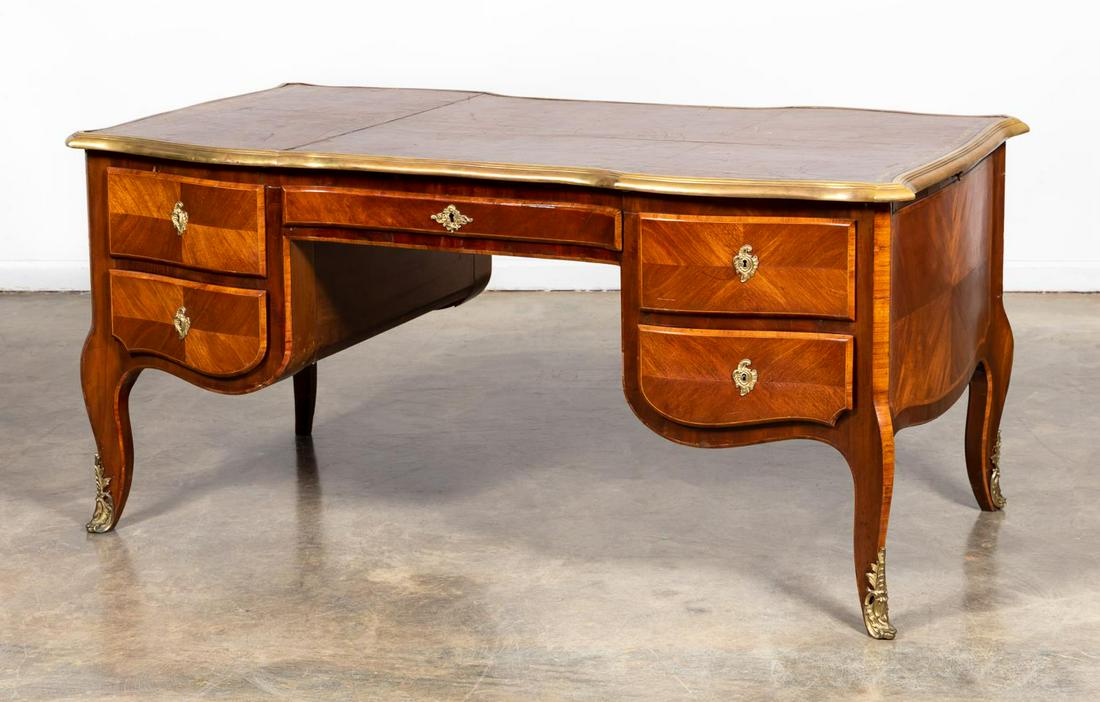 LOUIS XV STYLE LEATHER TOP FAUX PARTNERS DESK: Maison Gouffe (French), 20th Century. A Louis XV style partner's desk of mahogany, mahogany veneers and satinwood banding, with inset brown leather top, the top edge having an applied cast brass moldi