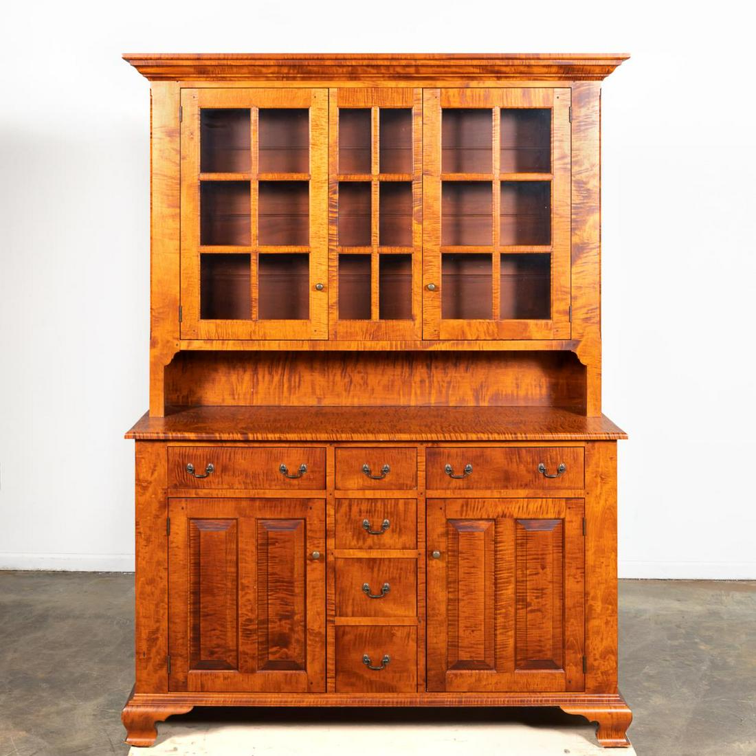 BENCH-MADE TIGER MAPLE STEP-BACK CUPBOARD: American, 20th century. A bench-made tiger maple step-back cupboard with cherry stained finish, of typical form with cornice top over glass display and open serving shelf, the cabinet base with 6 smal