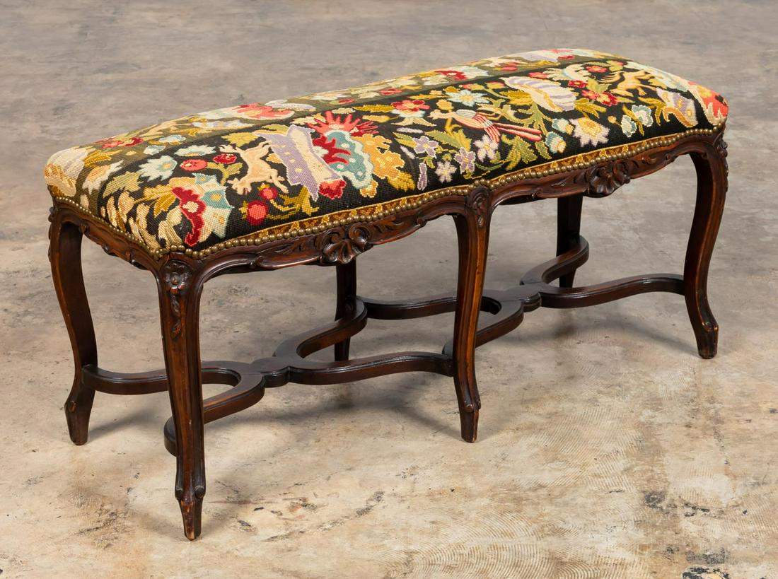 LOUIS XV CARVED BENCH, NEEDLEPOINT UPHOLSTERY: French or American, 20th century. French Louis XV style bench with hunt motif needlepoint upholstered top, the walnut frame carved with flowers and shells and having 6 cabriole legs joined by shaped s