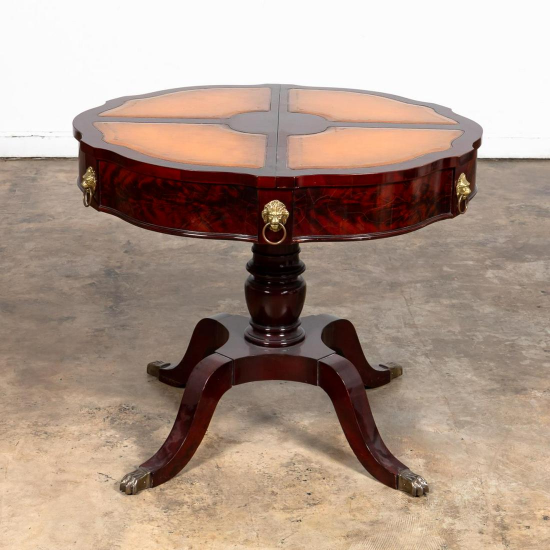 REGENCY STYLE LEATHER TOP DRUM TABLE: American, mid-20th century. Mahogany & mahogany veneer drum or center table, with shaped top having 4 inset butterscotch color leather panels, a conforming flame mahogany veneer frieze with brass lion