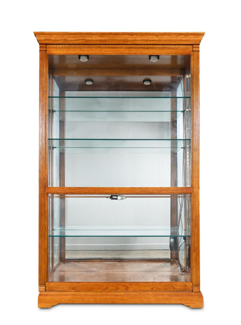 LARGE HOWARD MILLER OAK AND GLASS DISPLAY CABINET: Howard Miller, late 20th century. Large oak curio or display "Parkview" cabinet with dentil moulding, sliding front beveled glass door, the lighted interior fitted with four glass shelves. Plaque to t