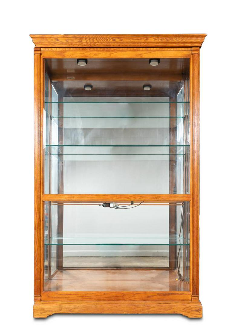 LARGE HOWARD MILLER OAK AND GLASS DISPLAY CABINET: Howard Miller, late 20th century. Large oak curio or display "Parkview" cabinet with dentil moulding, sliding front beveled glass door, the lighted interior fitted with four glass shelves. Plaque to t