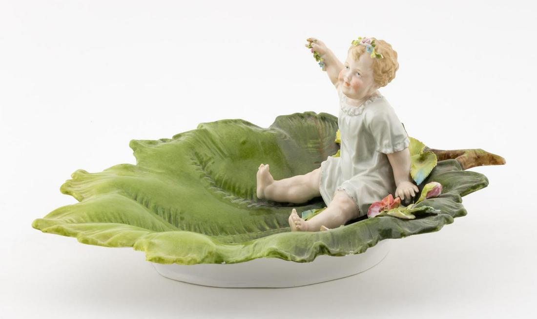 19TH C., MEISSEN BABY ON A LEAF PORCELAIN FIGURE: Meissen, 19th century. A porcelain fruit dish with a polychromed figural baby resting on a leaf. Marked to underside. Approx: h. 5.5", w. 9", d. 11.25".