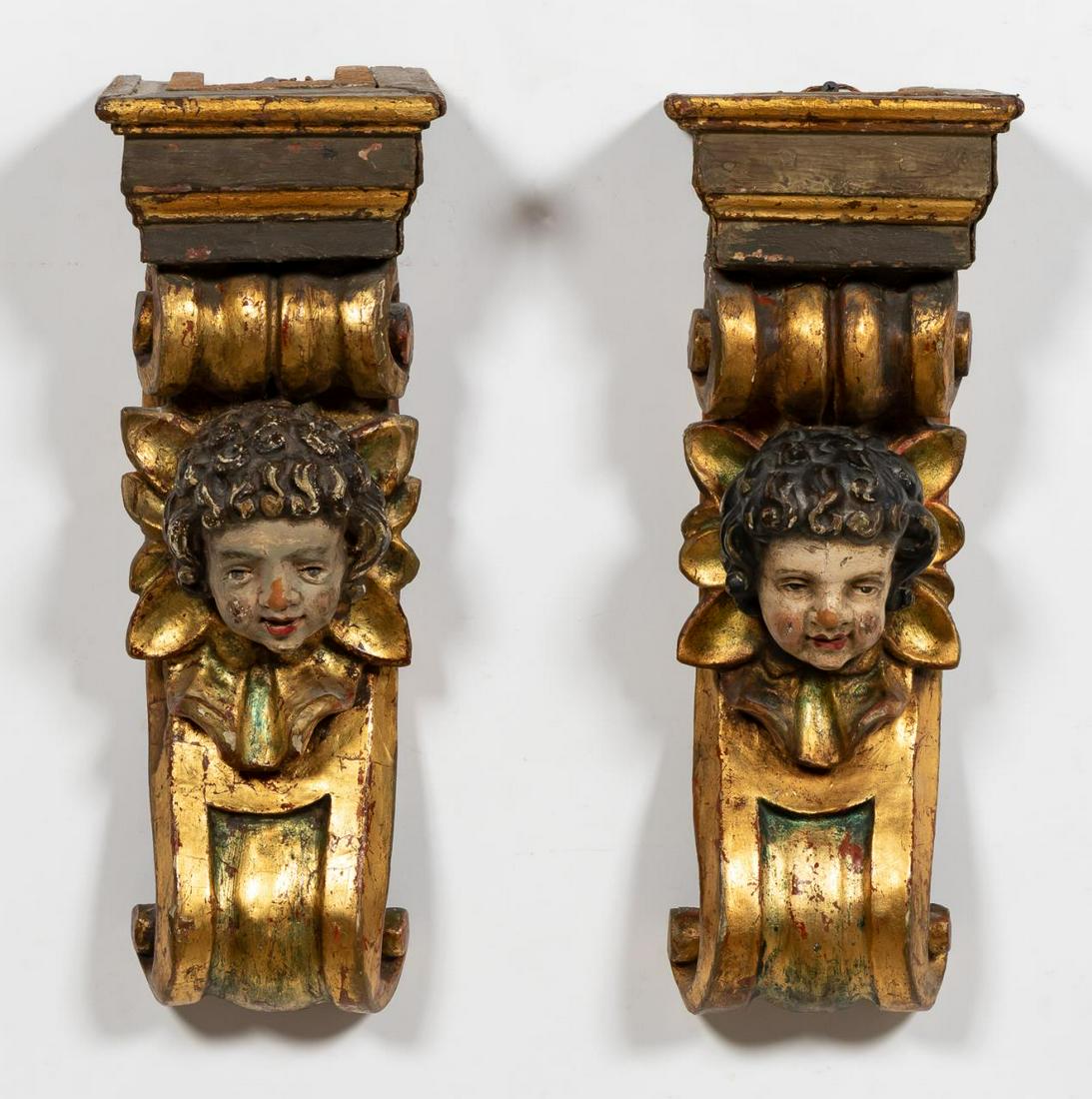 ITALIAN CARVED & POLYCHROMED GILTWOOD BRACKETS: Continental school, 20th century. Pair of carved brackets with gilded s-curves and polychromed putti heads supporting an entablature.Approx. h 17" w 6.25" d 4.25"