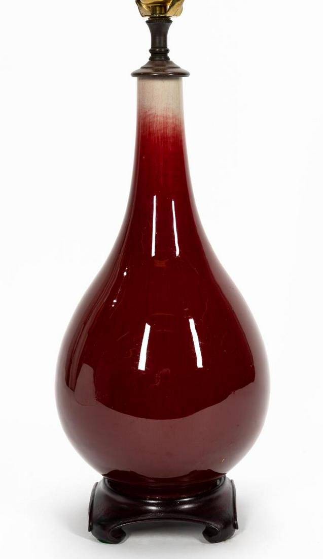 CHINESE OXBLOOD BOTTLE VASE MOUNTED AS A LAMP: Chinese. Oxblood sang de boeuf porcelain bottle form vase mounted as a single light lamp, on a curved wooden base, and with shade. Unmarked. Approx. overall 19.5", the body 13.5"