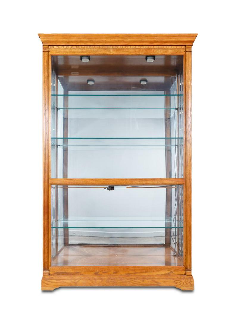 LARGE HOWARD MILLER OAK AND GLASS DISPLAY CABINET: Howard Miller, late 20th century. Large oak curio or display "Parkview" cabinet with dentil moulding, sliding front beveled glass door, the lighted interior fitted with four glass shelves. Plaque to t