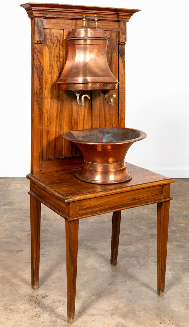 19TH C. CONTINENTAL COPPER LAVABO ON WALNUT STAND: Continental, 19th century. Copper and brass lavabo having a reservoir decorated with a bird and double spigots, flared basin, walnut stand with shaped cornice, paneled back, and rising on tapered legs