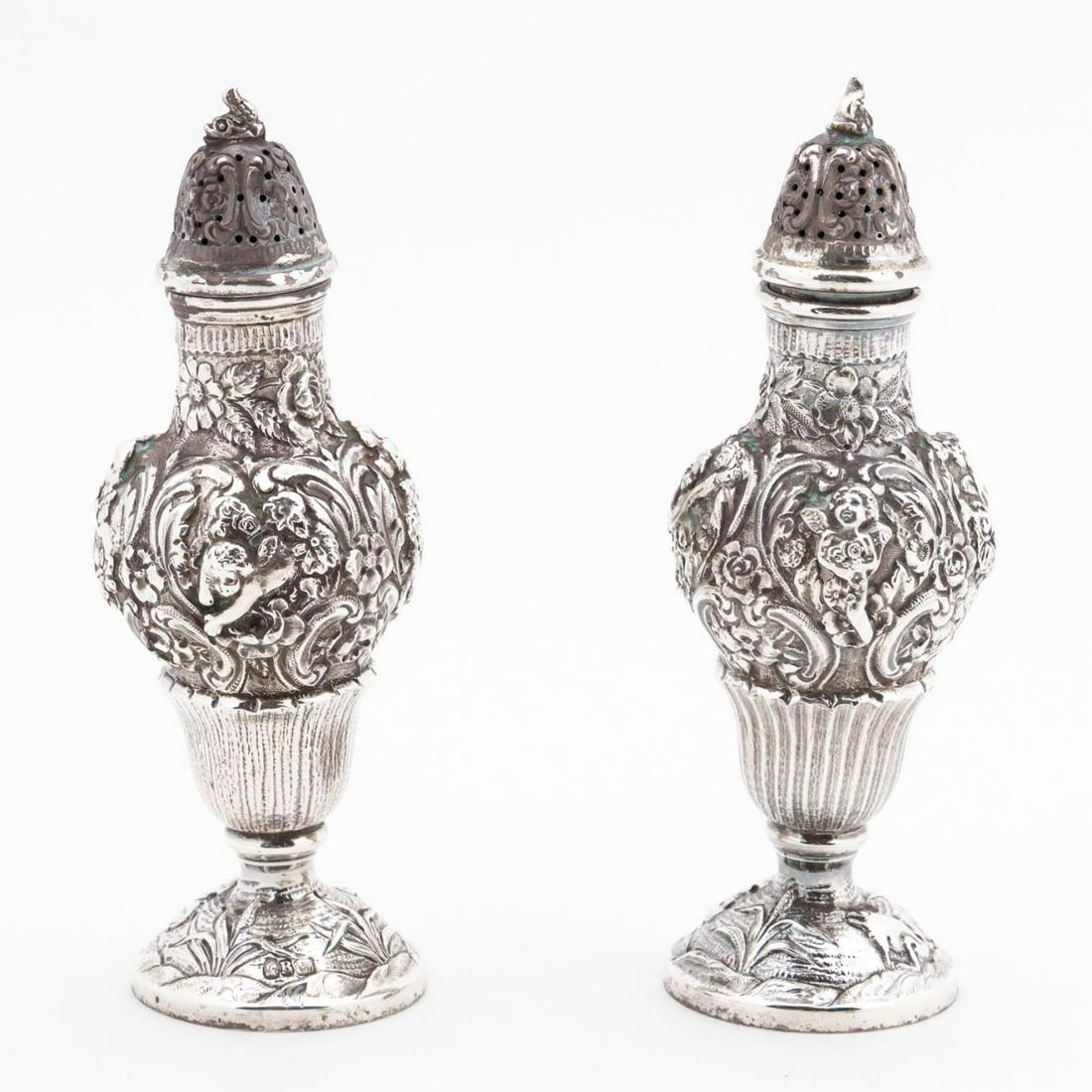PAIR CONTINENTAL .800 SILVER REPOUSSE CASTORS: Continental, 20th century, Pair .800 silver repousse putti and floral decorated castors with dolphins on lids. Marked with "Head", "B", "Lion", one on foot, one on rim of body, lids not marked. Approx