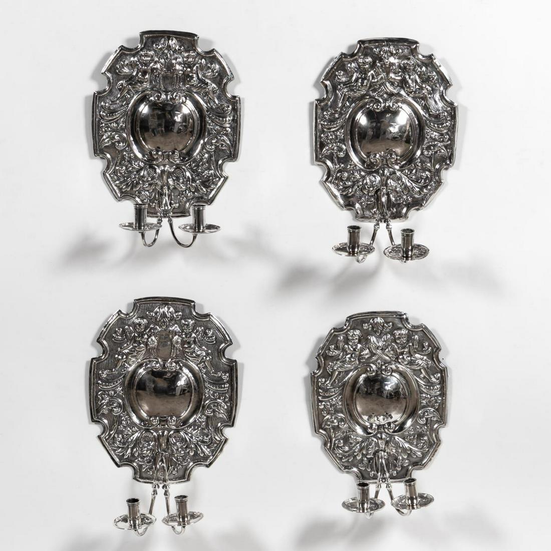 SET OF 4, SILVERPLATE WALL SCONCES, CONTINENTAL: Continental, 20th c. Set of four silverplate shield-shaped two-light sconces depicting two cherubs and scrolling foliate designs. Apparently unmarked. Approx. h. 15.5" w. 12" d. 7".