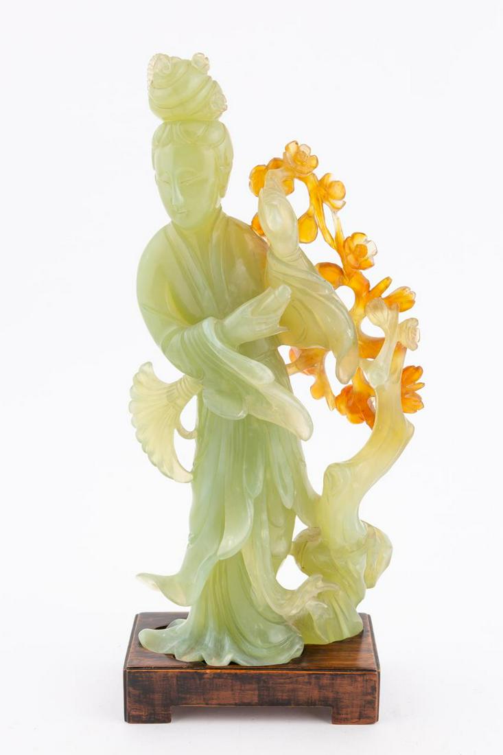 CHINESE JADE QUANYIN FIGURE ON WOOD STAND: Chinese. Carved jade and nephrite Guanyin figural sculpture on carved wood stand. Apparently unmarked. Approx. h. 11" (on stand), w. 5.25" (sculpture). Provenance: From the Estate of Jack Warner / The