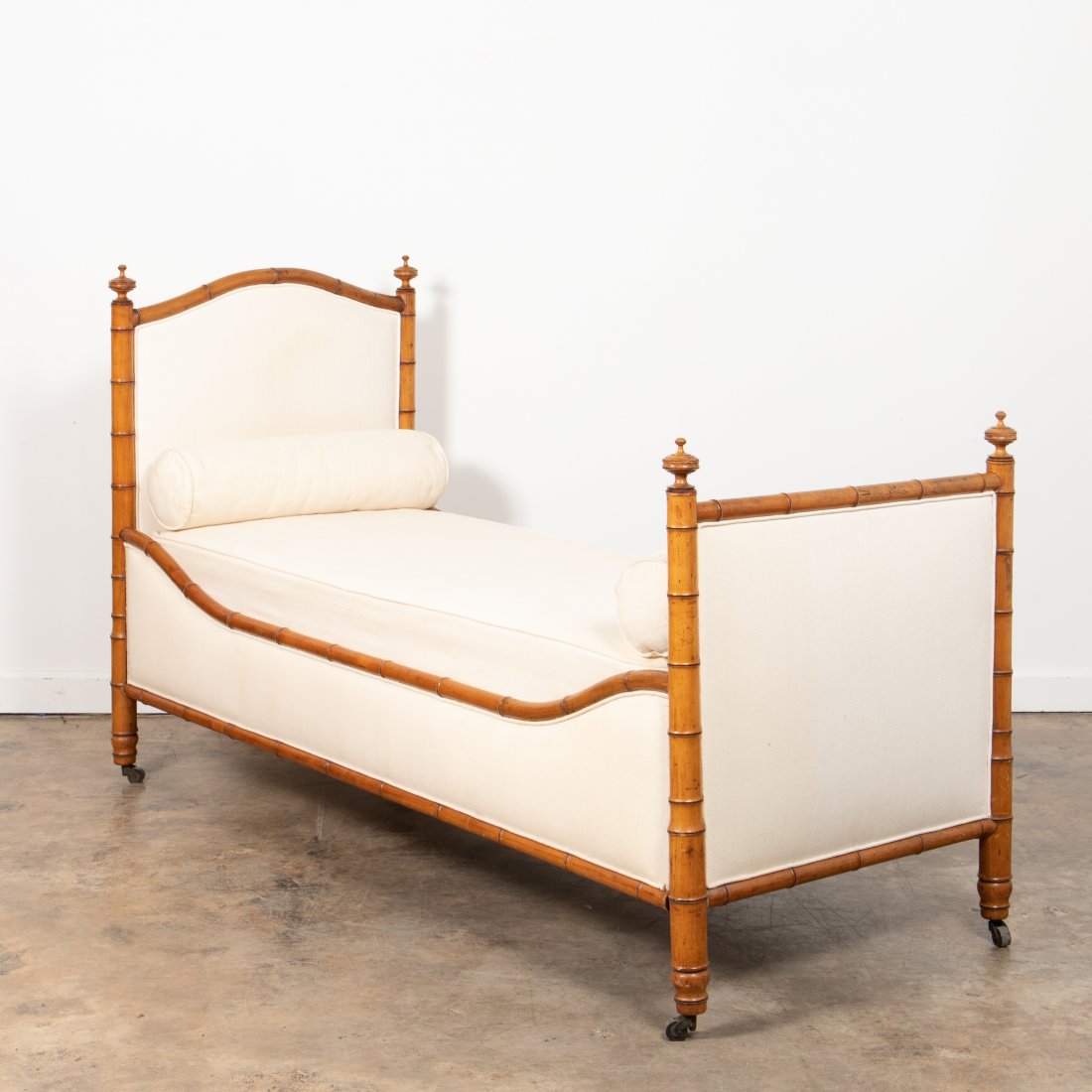 19TH C. FAUX BAMBOO TWIN BED WITH BOLSTER PILLOWS: Likely French, late 19th century. Victorian era aesthetic movement faux bamboo framed padded twin bed having an arched headboard, wooden side rails, and urn finials; together with mattresses and two b