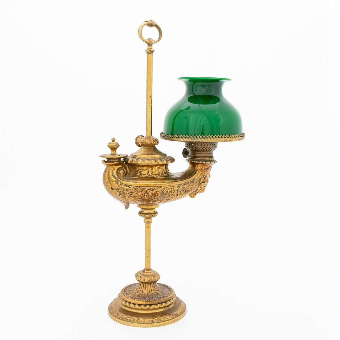 FRENCH BRASS STUDENT: French, circa 1900. Cast brass adjustable student's oil lamp, decorated with scrolled florals, masks and cartouches, cased green glass shade and colorless chimney, and rising on a patterned base. Mark