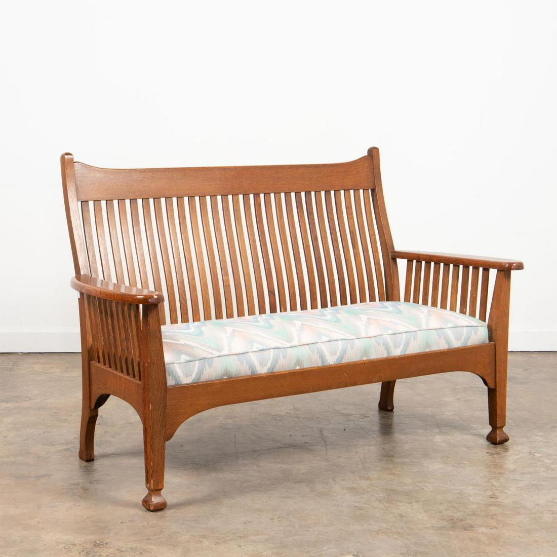 20TH C. AMERICAN ARTS AND CRAFTS STYLE OAK SETTEE: American Arts & Crafts oak slat back settee having a curved crest, drop in seat, and rising on front tapered legs. Unmarked. Approx. h. 39", w. 59.25", d. 24.5".