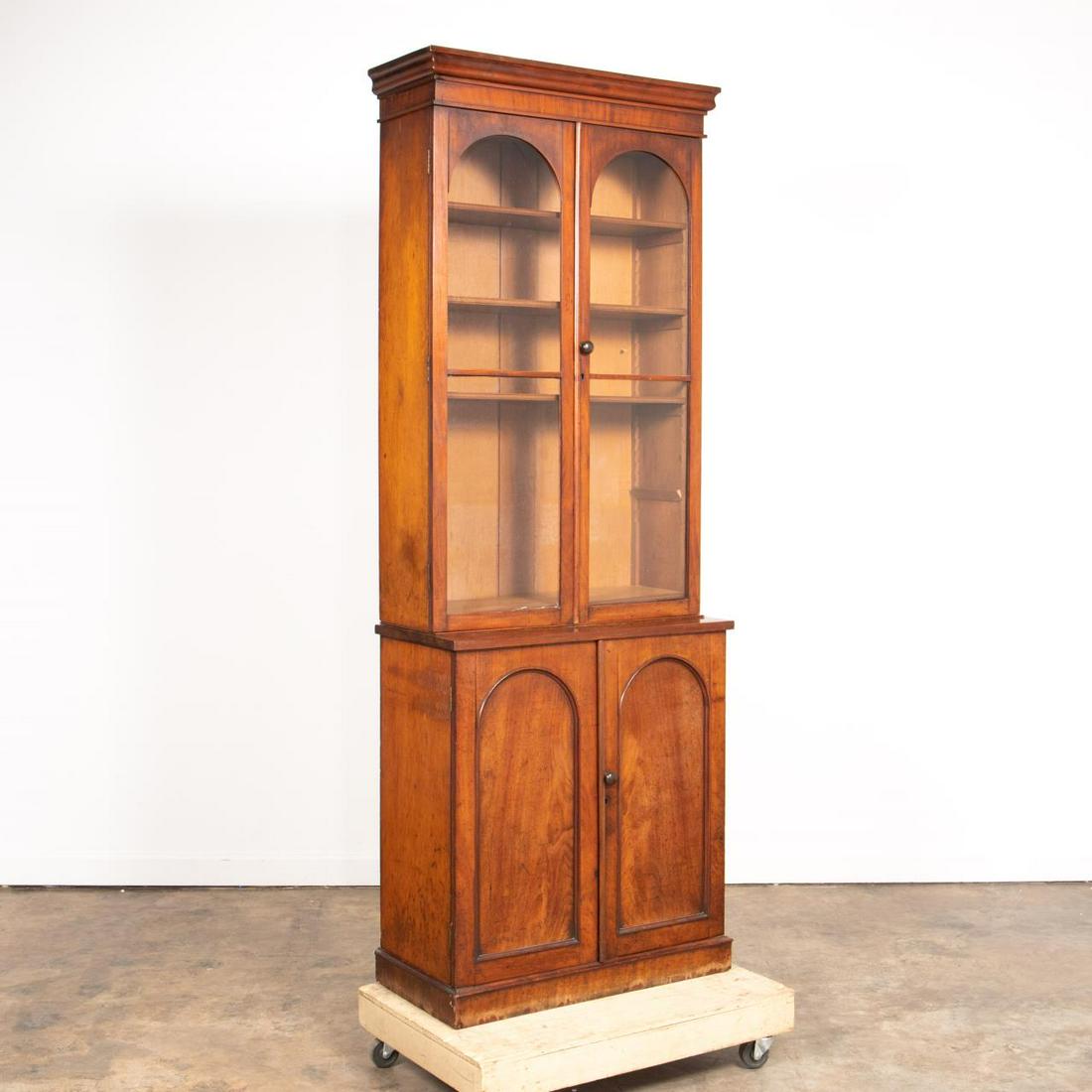19TH C. ENGLISH VICTORIAN MAHOGANY BOOKCASE: English, 19th century. Victorian era mahogany bookcase having a shaped cornice with double doors below with arched glazing, the lower case with double doors with arched panels, and rising on a plinth 