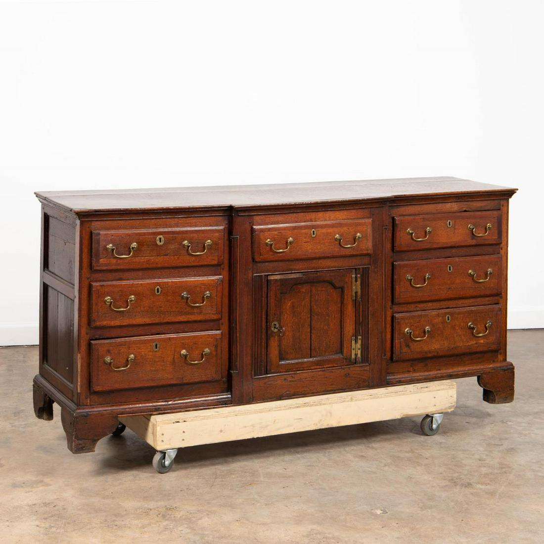 18TH C. GEORGIAN OAK SERVER OR DRESSER: English, 18th century. Provincial Georgian oak server or dresser having an overhanging top with shaped cornice, center drawer with paneled door below, flanked by six drawers, and rising on bracket fee