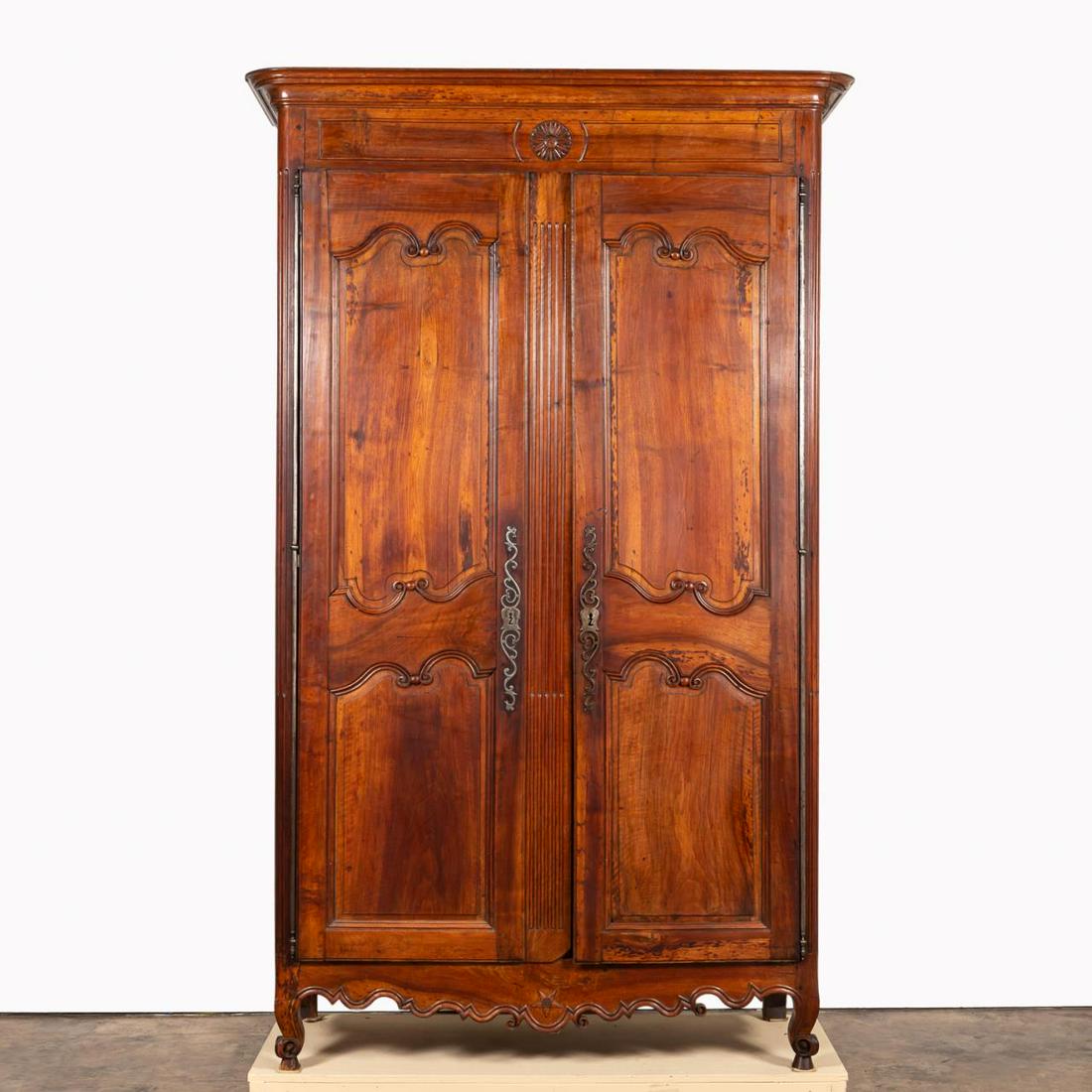 18TH C. LOUIS XV PROVINCIAL CARVED WALNUT ARMOIRE: French, 18th century. Carved walnut Louis XV provincial armoire, having a shaped cornice, sunflower rosette, double paneled doors and sides, interior fitted with shelves and two drawers, scalloped apr