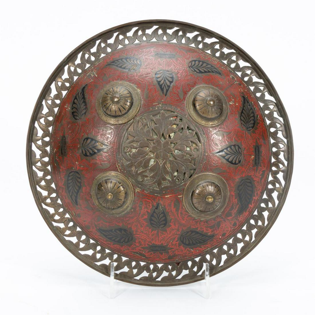 19TH C. PERSIAN CONVEX RED ENAMELED SHIELD: Iranian, 19th century. Persian convex brass red and black enamel shield with pierced border, bosses, and foliate motif. Apparently unmarked. Provenance: Acquired from Czerny's International Auction Ho