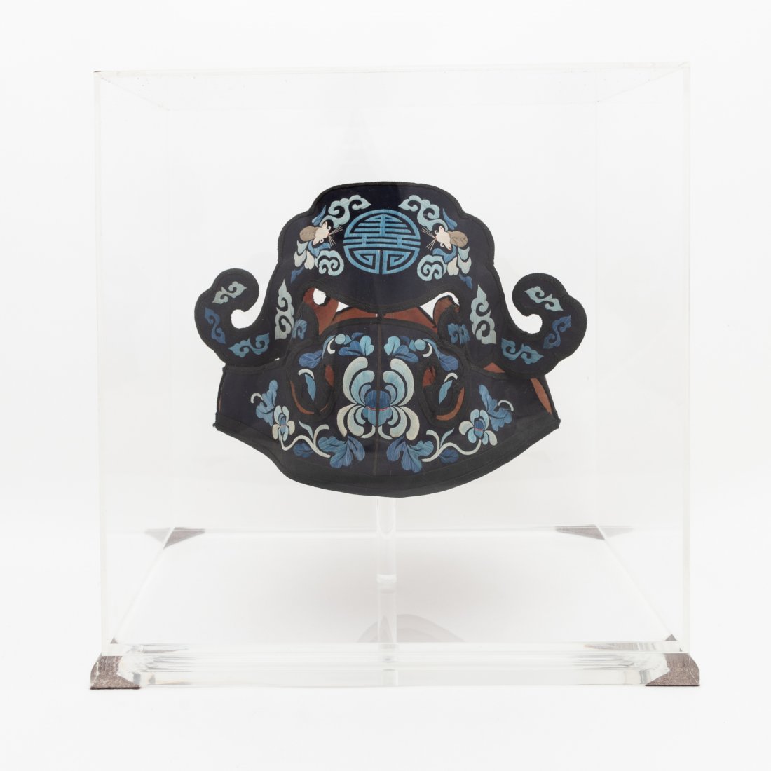 CHINESE CHILD: Chinese. Blue and black embroidered silk child's hat having a mythical animal form with floral detail and shou, in an acrylic case. Unmarked. Approx. h. 7.5", w. 9.75" (hat); h. 12.75", w. 12.5", d. 8