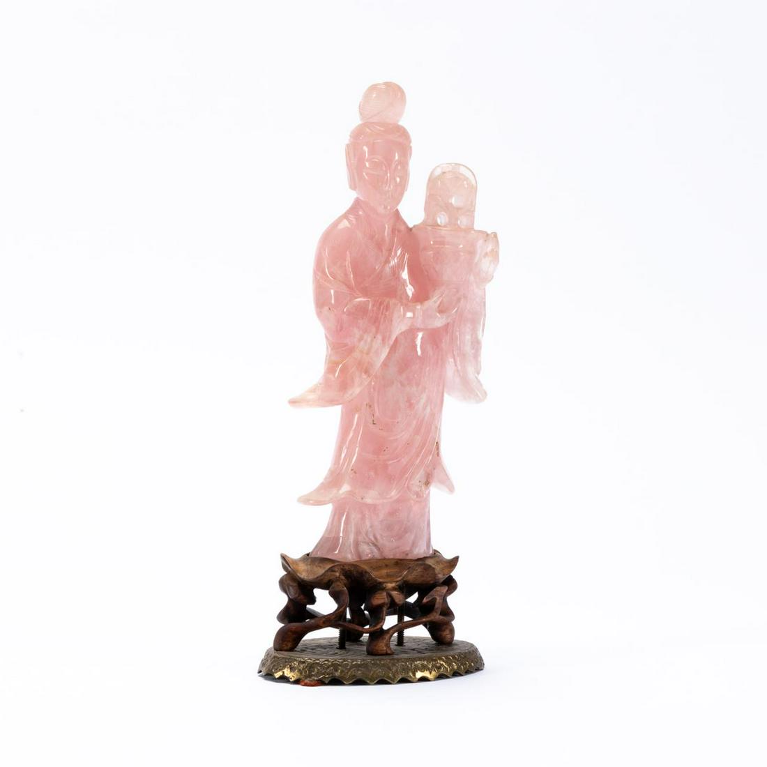 CHINESE ROSE HARDSTONE STANDING QUANYIN ON BASE: Chinese. Rose quartz type hardstone figure of a standing Quanyin on wooden and metal base. Unmarked. Approx. h. 8" (figure); h. 9.75" (overall).