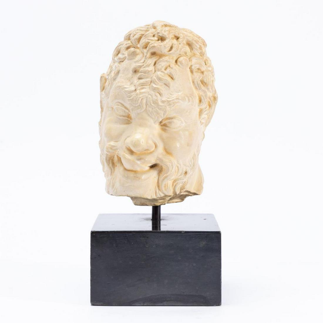 AFTER THE GREEK ANTIQUE, CAST HEAD OF A SATYR: Likely American, mid-20th century. After the Hellenistic, 2nd century, cast plaster or manufactured stone fragment of the head of a mischievous satyr, on a black wooden base. Unmarked. Approx. h. 11",