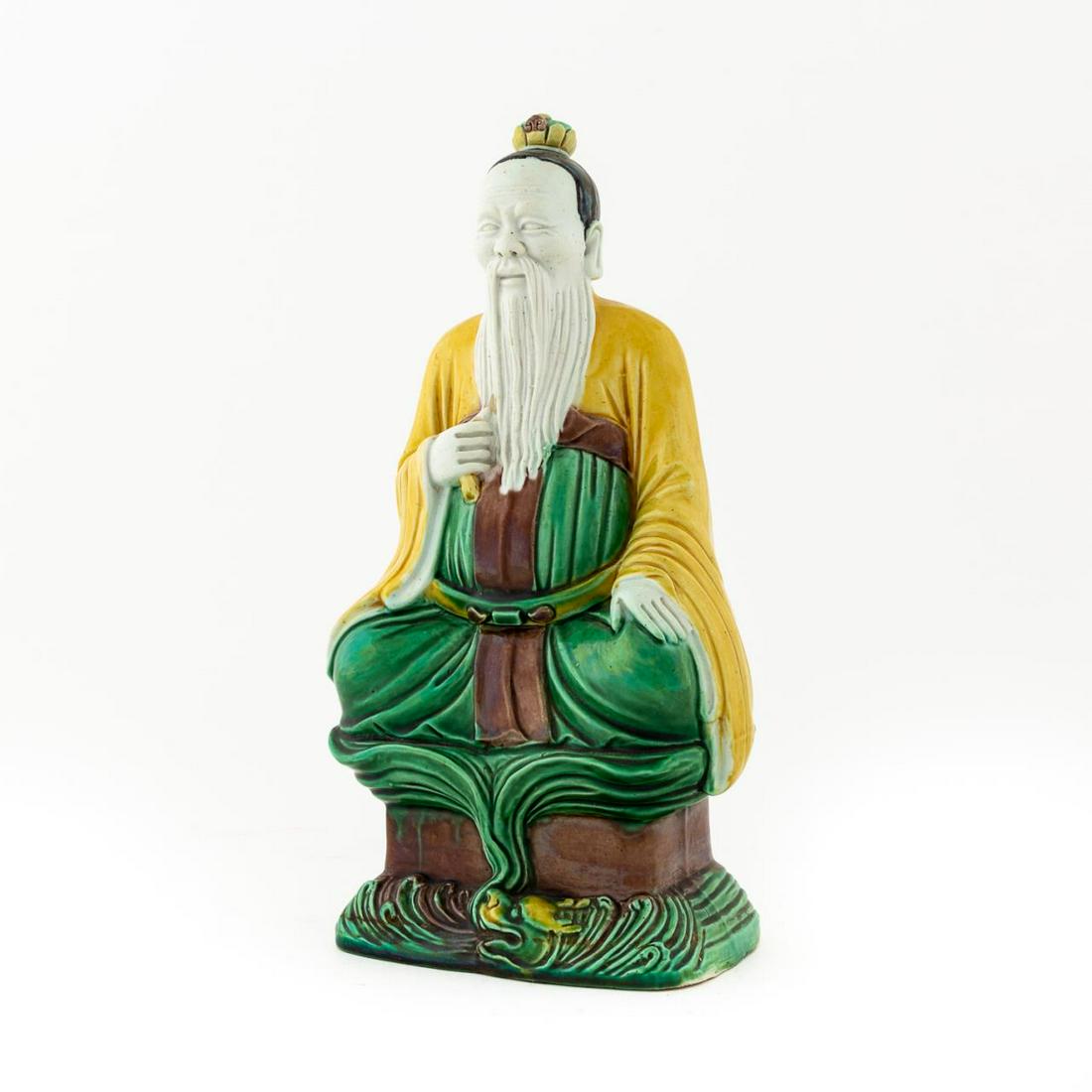 CHINESE SANCAI GLAZED SEATED MALE FIGURE: Chinese. Sancai glazed seated male ceramic figure with long beard and resting over dragon flame. Apparently unmarked. Approx. h. 10.125".