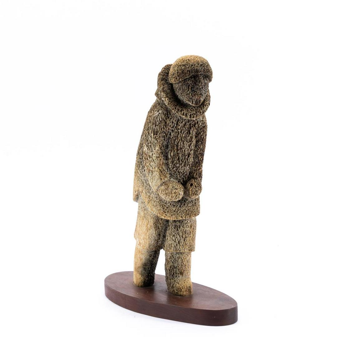 INUIT FOSSILIZED WHALE BONE FIGURAL SCULPTURE: Inuit folk art carved fossilized whale bone sculpture of walking male figure. Apparently unmarked. Approx. h. 13.875" (on base), w. 11" (base).