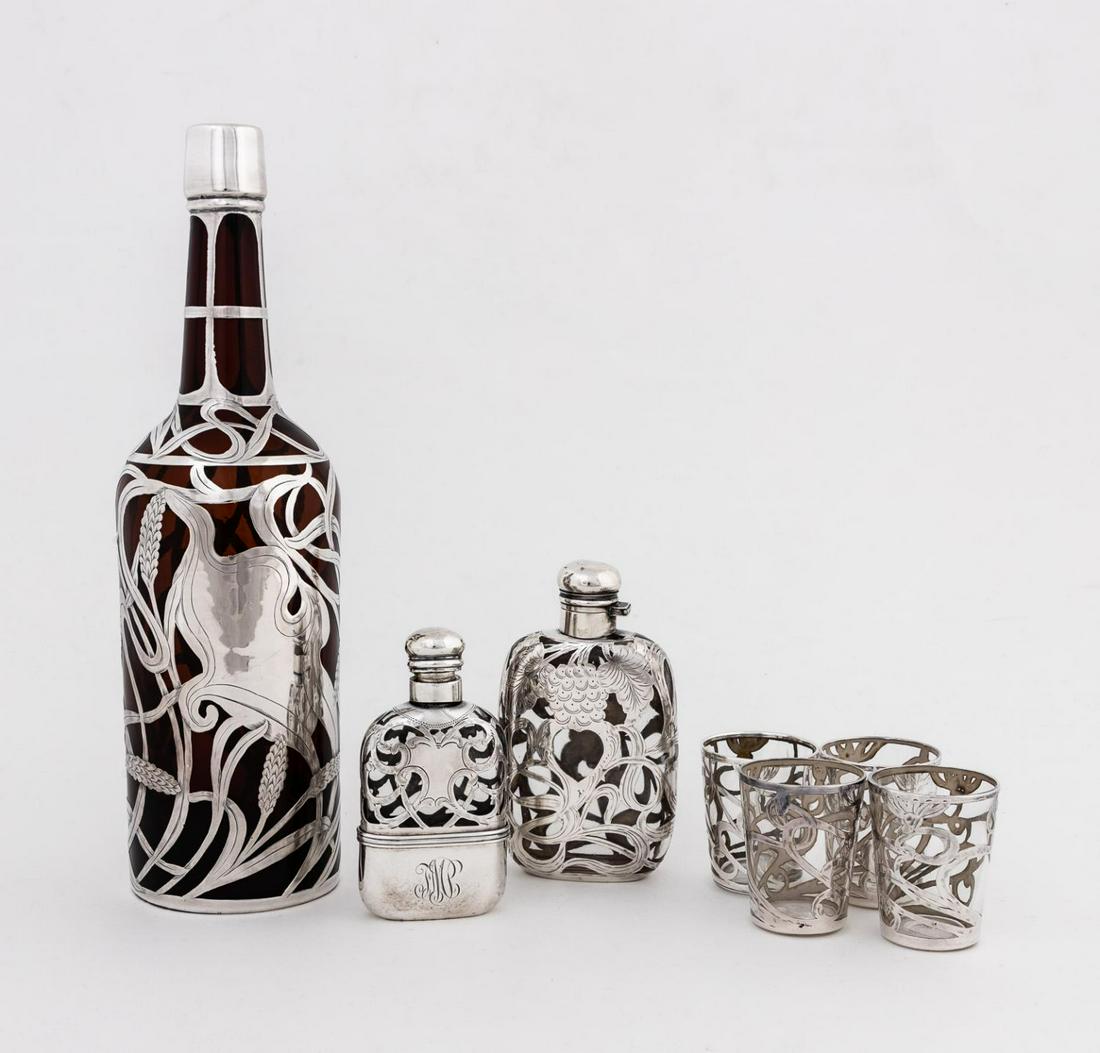SEVEN SILVER OVERLAY BARWARE PIECES: American and Continental, early 20th century. Seven piece group of silver overlay, comprising of two flasks, four shot glasses, and one amber glass bottle form decanter without a stopper. Three marked