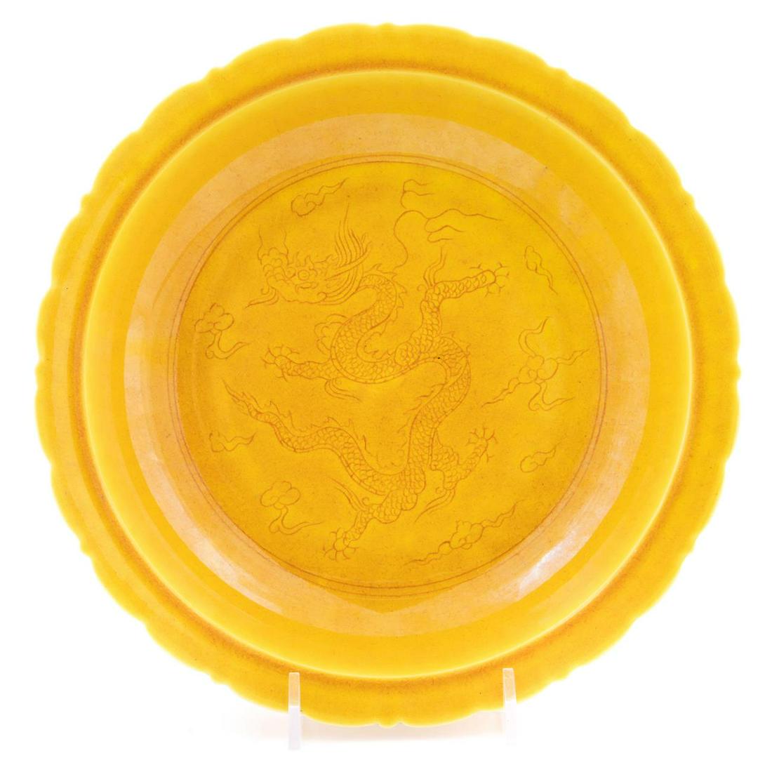 CHINESE YELLOW GLAZE INCISED DRAGON MOTIF BOWL: Chinese yellow glaze porcelain bowl, having a scalloped rim and well with incised decoration depicting a dragon chasing a flaming pearl surrounded by bats, with a blue six character Hongzhi type mark 