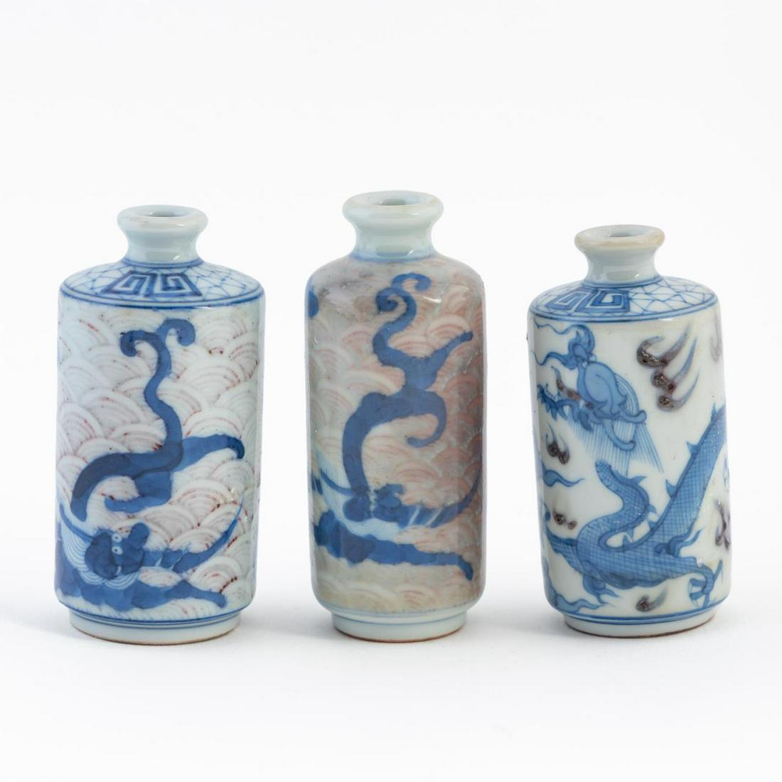 3 CHINESE BLUE, WHITE, AND IRON RED SNUFF BOTTLES: Three Chinese blue, white, and iron red snuff bottles, each of cylinder form with a short neck and recessed foot, decorated in the round with dragons and flying fish, having no apparent mark. Tallest: