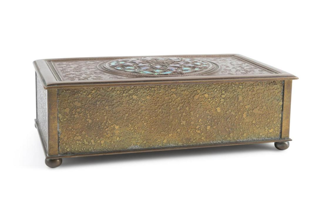 L. C. TIFFANY FURNACES GILT BRONZE & ENAMEL HUMIDOR: Louis C Tiffany Furnaces gilt bronze and enamel humidor, ca 1925, of rectangular form centering a floral reserve with multi-color enamel on a textured gilt bronze ground, raised on bun feet, the under