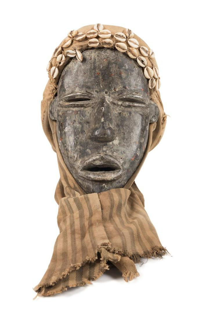 DAN PEOPLES CARVED WOODEN MASK W/ HEADDRESS: Dan peoples carved wooden mask with headdress, Ivory Coast or Liberia, mid to late 20th century, having a conical burlap striped ticking, and cowrie shell headdress above the oval carved and painted m