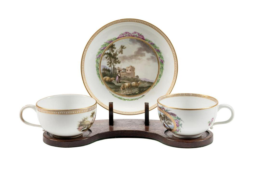 TWO MEISSEN CABINET TEA CUPS AND SAUCER WITH STAND: Three pieces of Meissen (German 1710) gilt trimmed porcelain cabinet tableware, 18th and 19th/20th century, comprising; a Marcolini era teacup having a reserve bordered by a ribbon tied floral garland