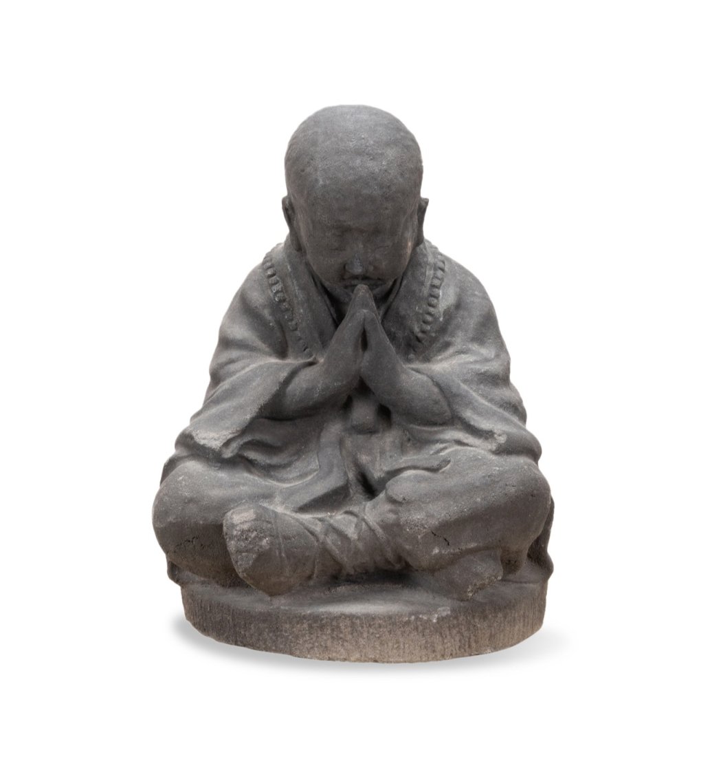 VOLCANIC ASH SCULPTURE OF A BUDDHIST MONK: Volcanic ash sculpture of a Buddhist monk, the monk depicted seated with his head bowed and hands in an altitude of prayer, wearing a mala and robe, the whole resting on a circular integral base. Appr