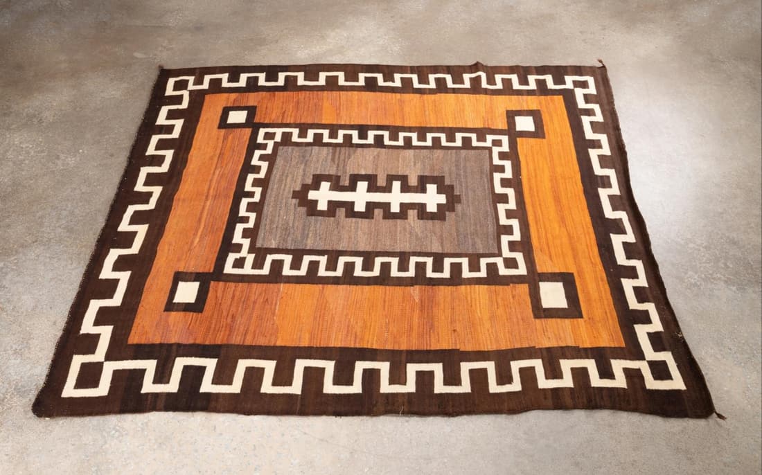HAND WOVEN WOOL DINE (NAVAJO) RUG, LIKELY GANADO: Hand woven wool Dine (Navajo) rug, likely Ganado, centering a joined cross in cream on a grey heathered ground, framed by a chocolate brown border with a cream Greek key design and a square at teach c