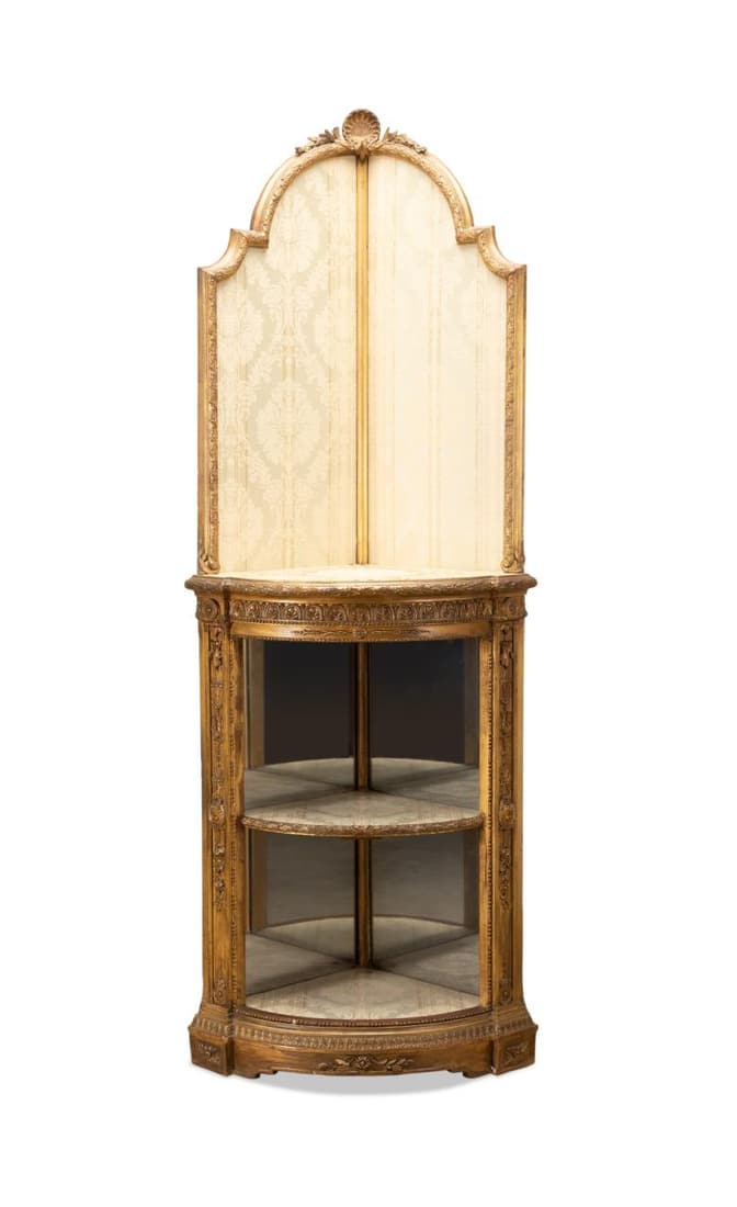LOUIS XVI STYLE GILTWOOD CORNER CABINET: Continental giltwood corner cabinet in the Louis XVI Neoclassical taste, with an arched upholstered upper section with shell crest and mirrored lower section with anthemion frieze, having no apparent 