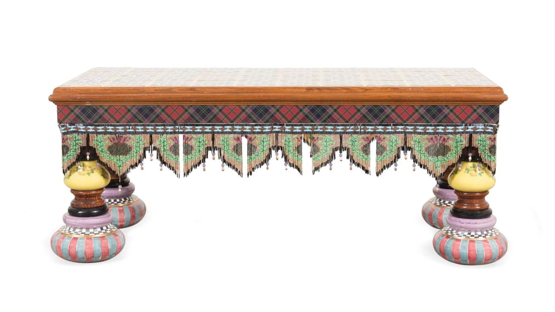 MACKENZIE-CHILDS TILE TOP TABLE WITH BEADED FRINGE: Mackenzie-Childs (American 1983), low table, having a rose patterned tile top, tartan apron, glass bead fringe, and rising on polychrome painted patterned Majolica legs, manufacturer's tag to the unde