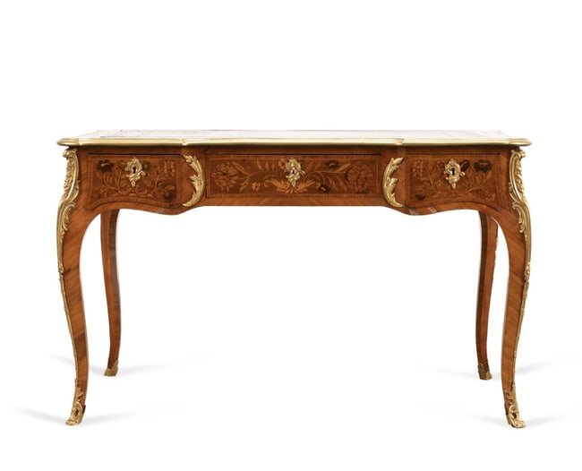 LOUIS XV STYLE BRONZE MOUNTED BUREAU PLAT: Louis XV style bureau plat, having a rectangular top with floral marquetry framing a leather writing surface, the top having a shaped banded brass edge, surmounting a wide apron with three frieze draw
