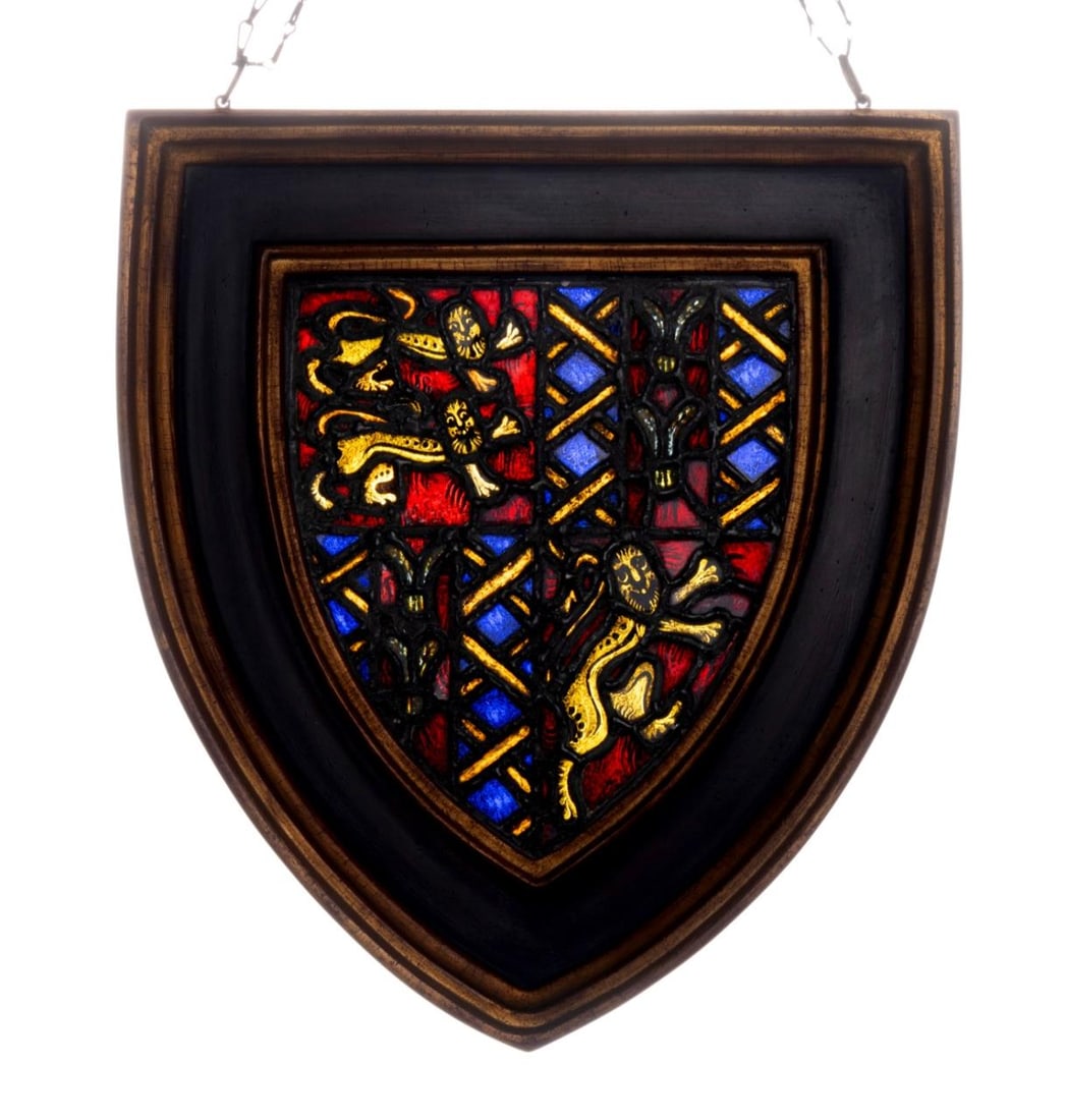 SHIELD FORM STAINED GLASS PANEL: Shield form stained glass panel, either a crest or family coat of arms, having two lions passant guardant in gold on red, and a lion rampant, framed, with attached chain for hanging. Provenance: From 