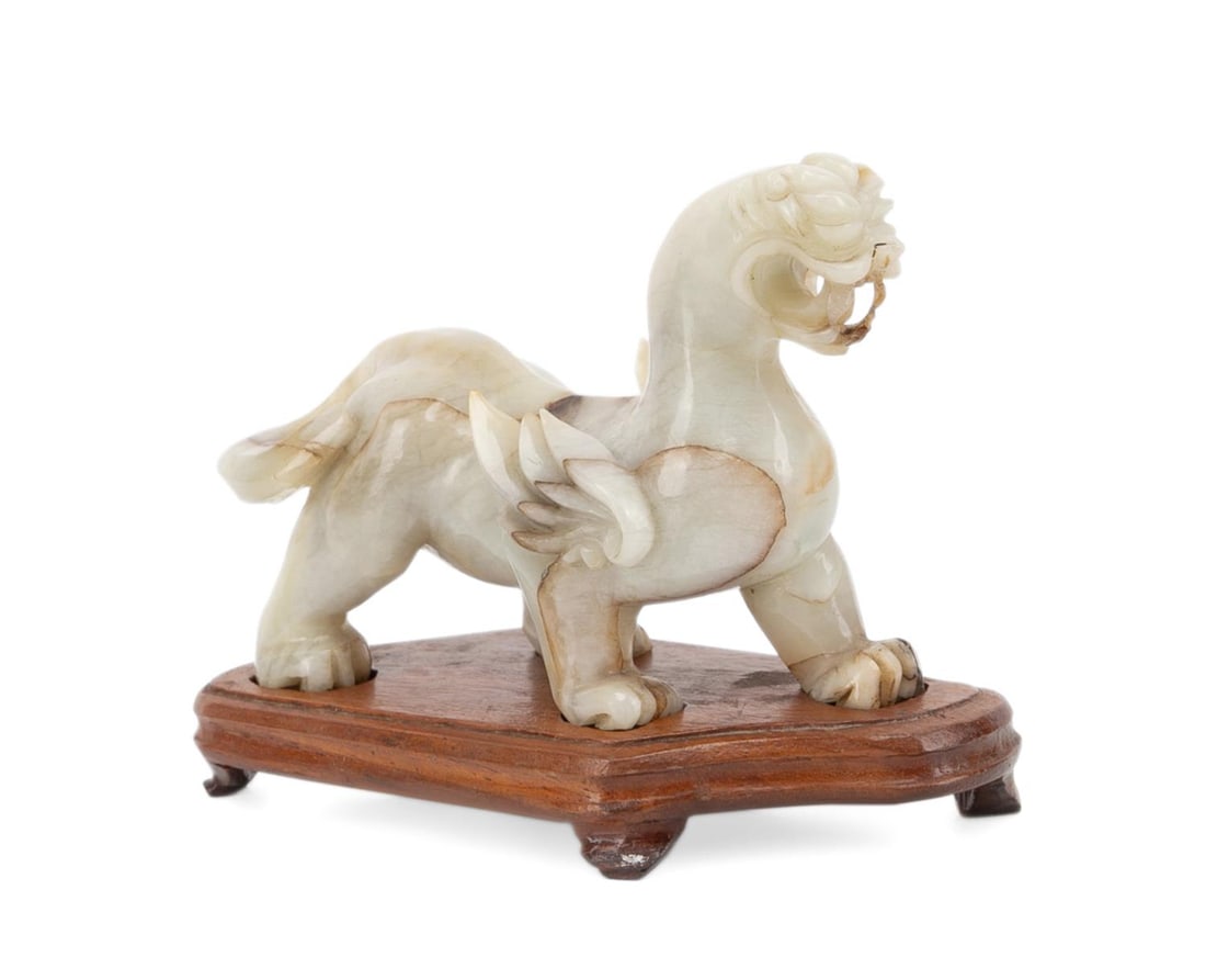 CHINESE PALE NEPHRITE CARVED MYTHICAL BEAST: Chinese. White and Russet nephrite Qilin or mythical beast carved figure on stand, apparently unmarked. Approximate dimensions: on stand h. 4.125", stand w. 5.875", stand d. 2.5". Provenance: The Esta