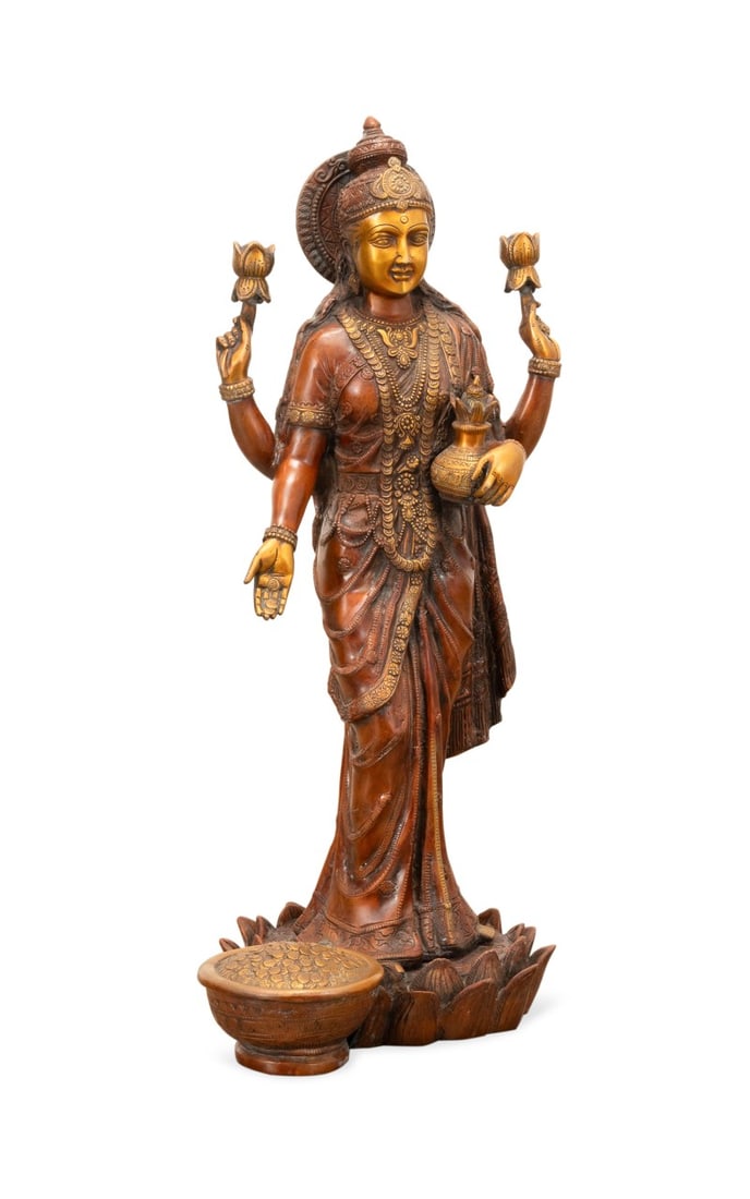 BRONZE HINDU FIGURE OF LAKSHMI: Southeast Asian. Bronze figure of Lakshmi, depicted standing on a lotus base, adorned with an elaborate headdress and layered jewelry, her four hands holding a kalasha (pot), two blooming lotuses, and