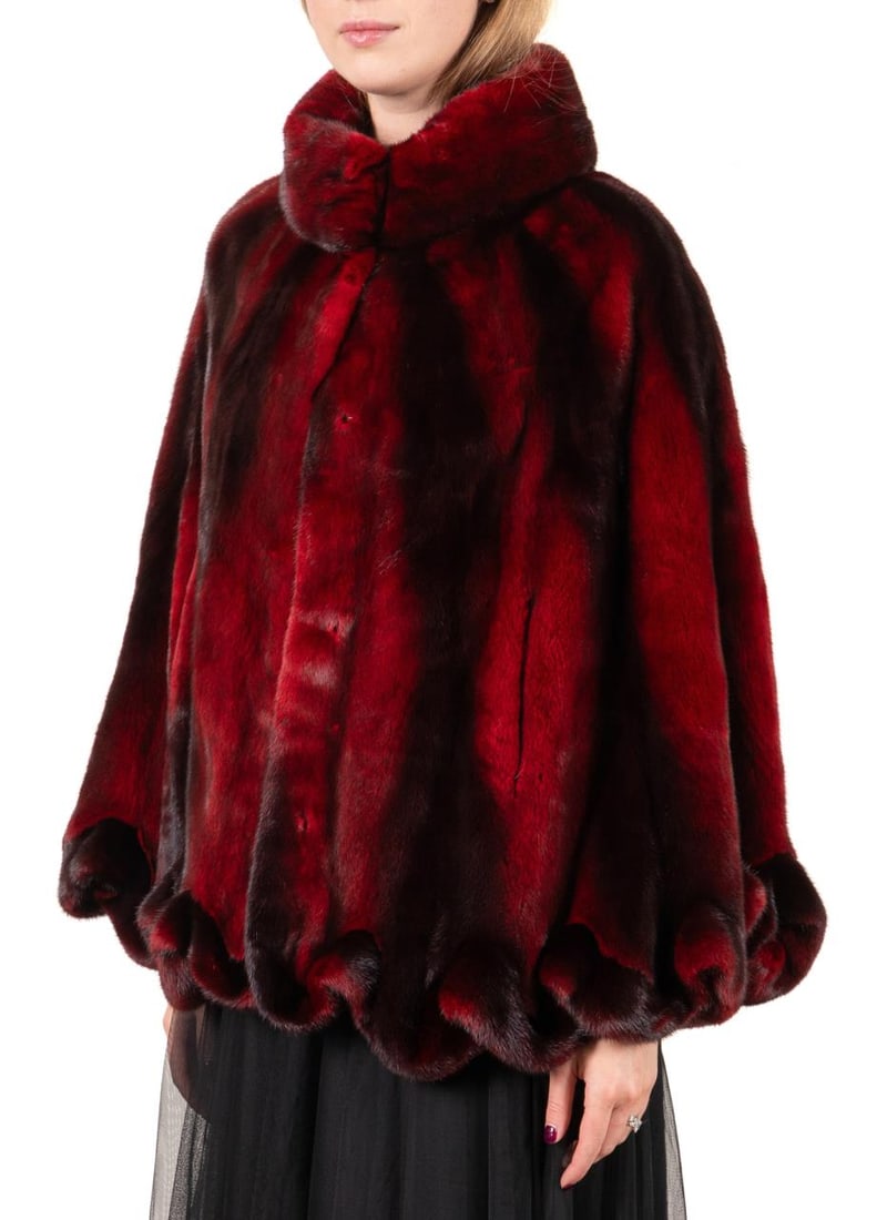 LADIES WINE RED MINK FUR RUFFLED CAPE: Wolfie (Canadian, founded 1974). Ladies wine red mink fur cape or capelet, having hook and eye closures, two outer pockets, and a ruffled hem, label and retail tags to the lining. Approx dimensions: f
