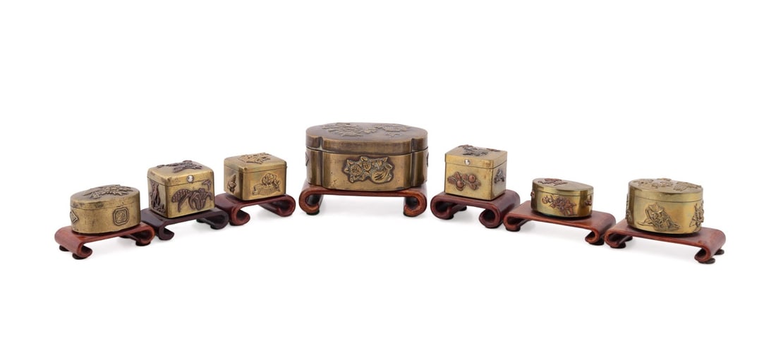 SEVEN JAPANESE MINIATURE METALWORK BOXES: Japanese, likely Meiji period. Seven miniature mixed-metal decorative boxes, with various floral motifs worked in high-relief takazogan, apparently unmarked. Each box is accompanied by a wooden stand.